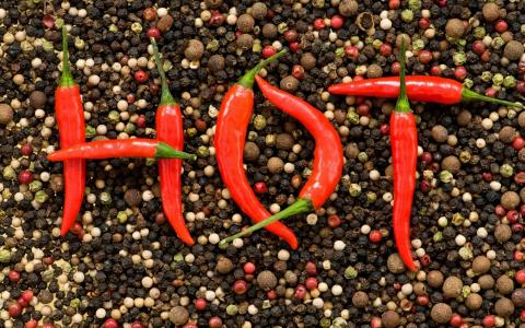 红色，黑色和白色的胡椒粉倒在桌子上，红辣椒的豆荚上放着HOT字样，这在俄语中意味着锋利而热烈，然而，热的照片。